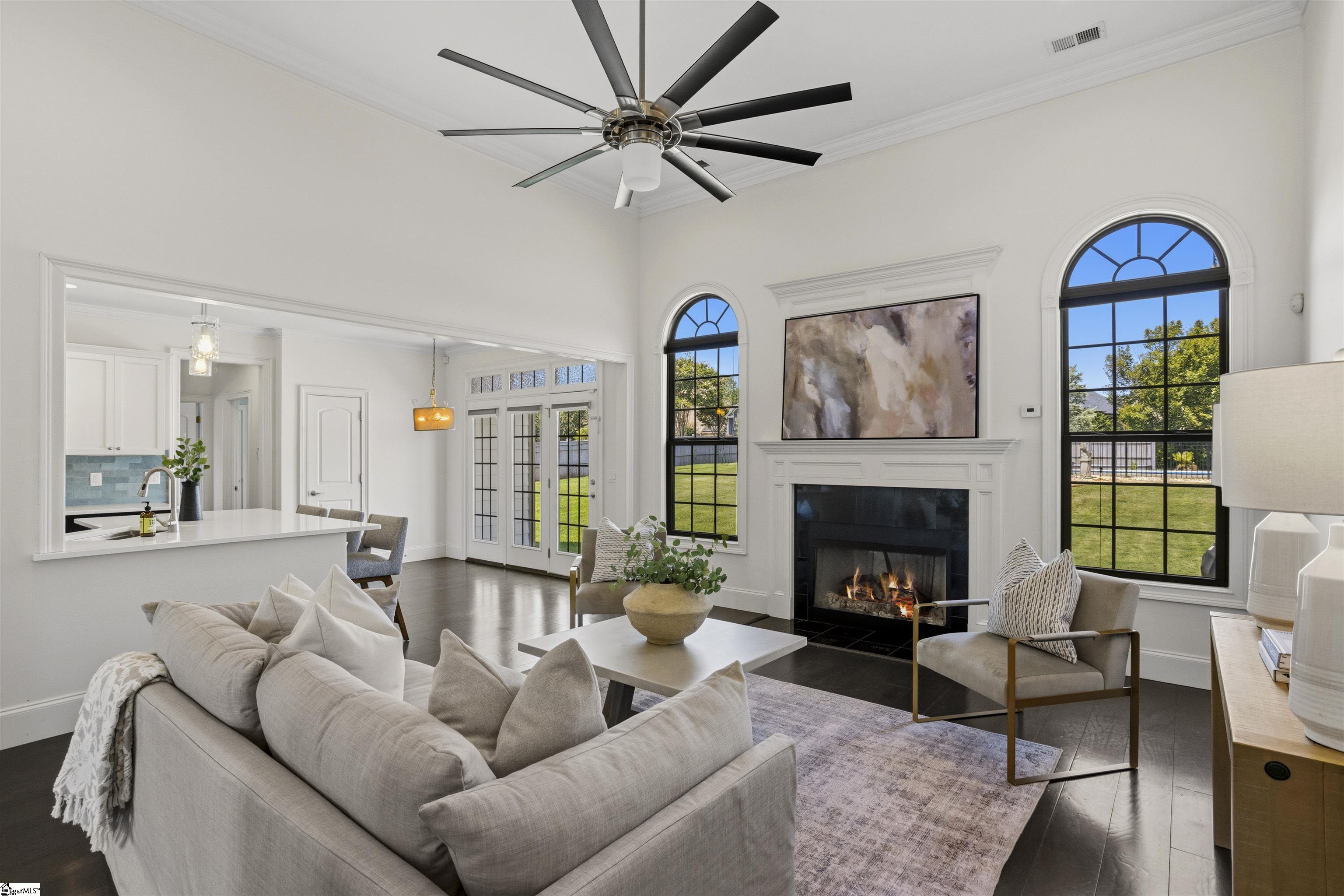 Staged living room with a fireplace, tall arched windows, and views of the backyard and pool.
