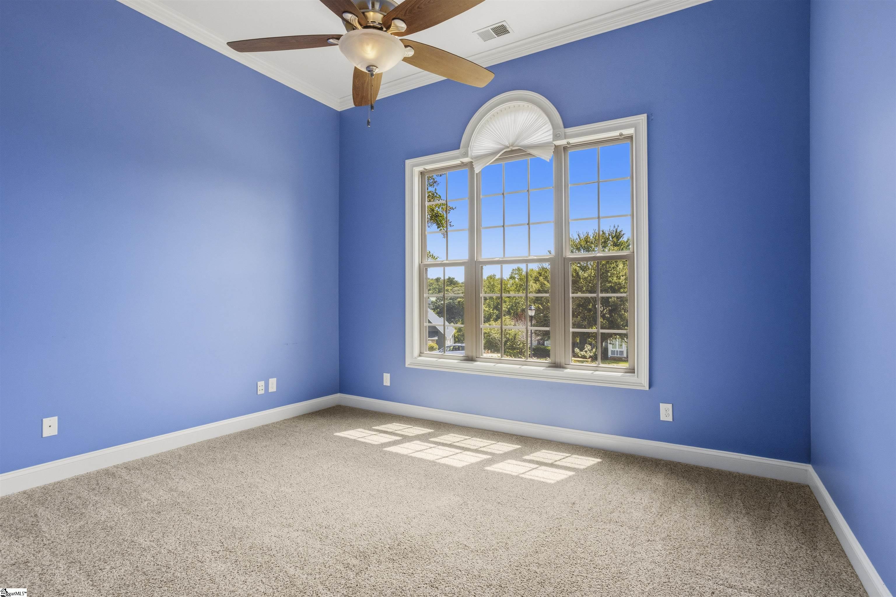 Empty blue room with beige carpet, a ceiling fan, and a large arched window.