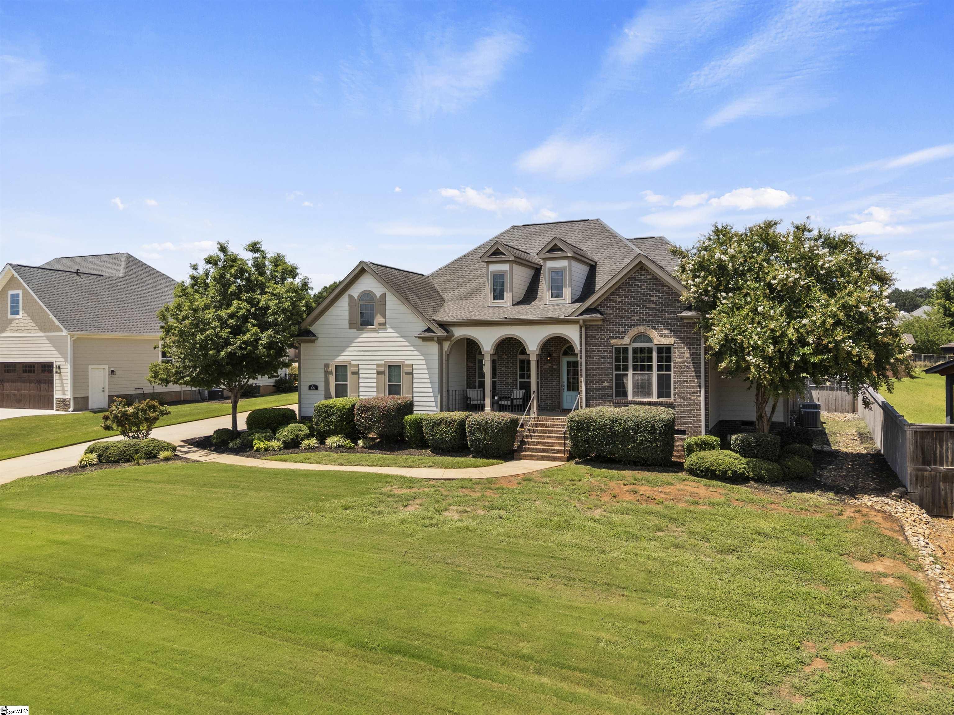 Two-story brick and siding home with an arched front porch, dormers, and a broad green lawn.