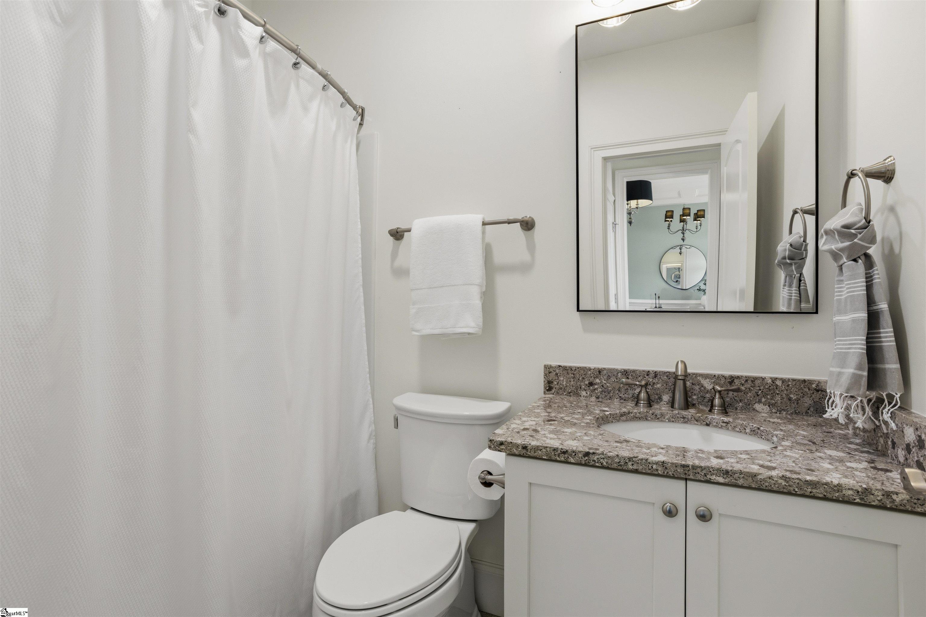 Bathroom with granite vanity, large mirror, and white shower curtain.