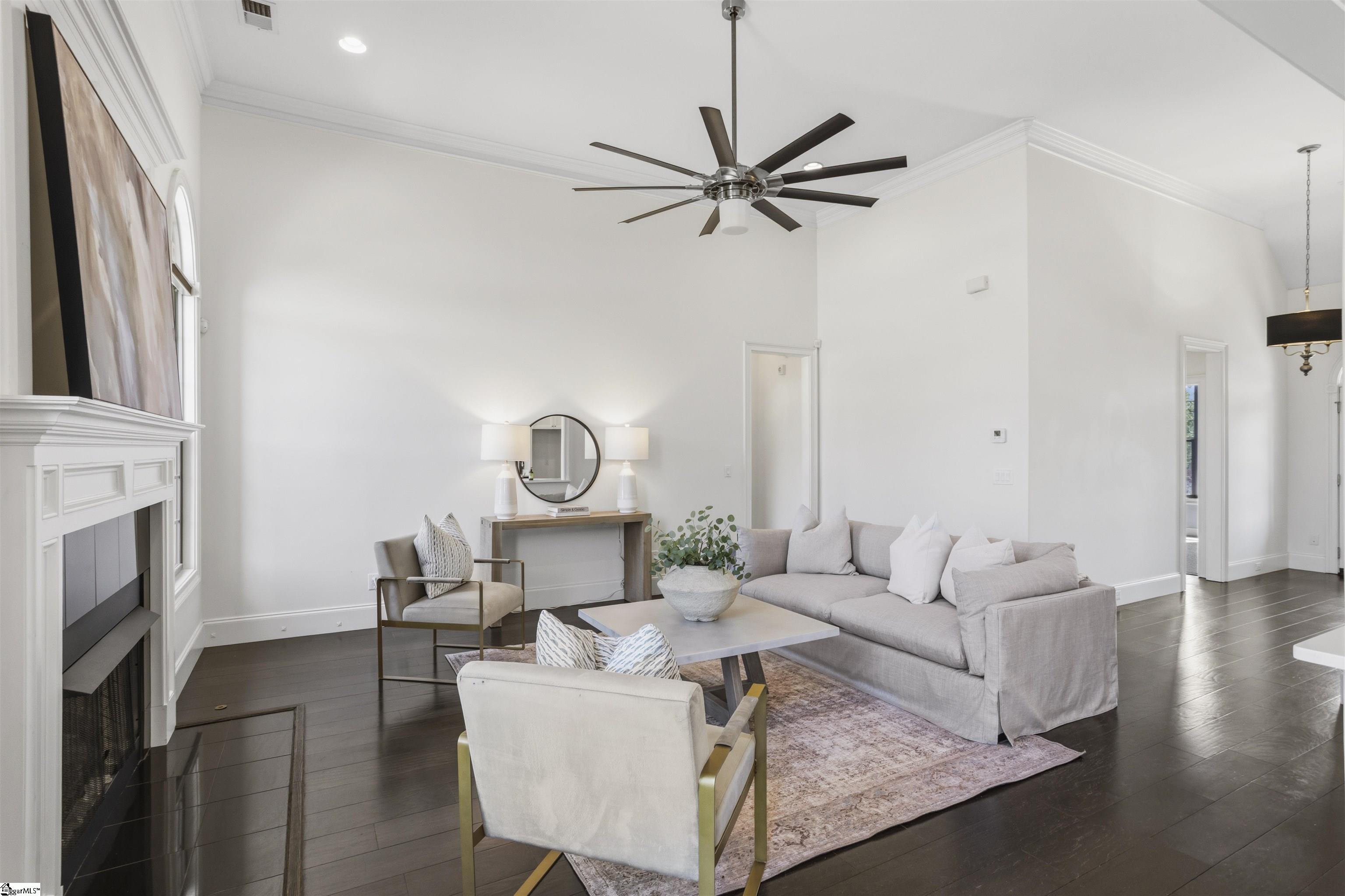 Staged living room with a white fireplace, high ceiling, gray sofa, and dark hardwood floors.