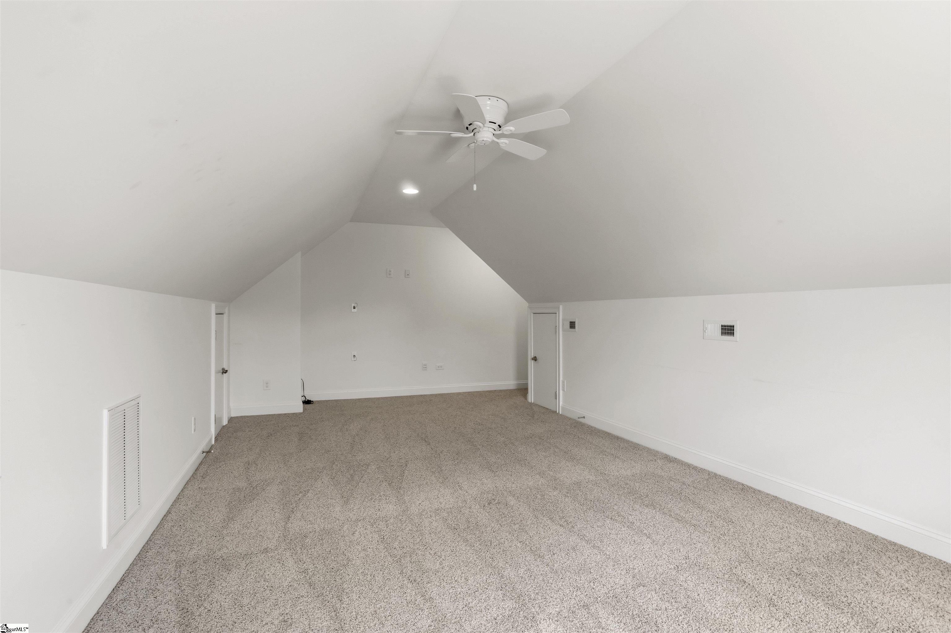 Empty carpeted room with a high sloped ceiling and ceiling fan.