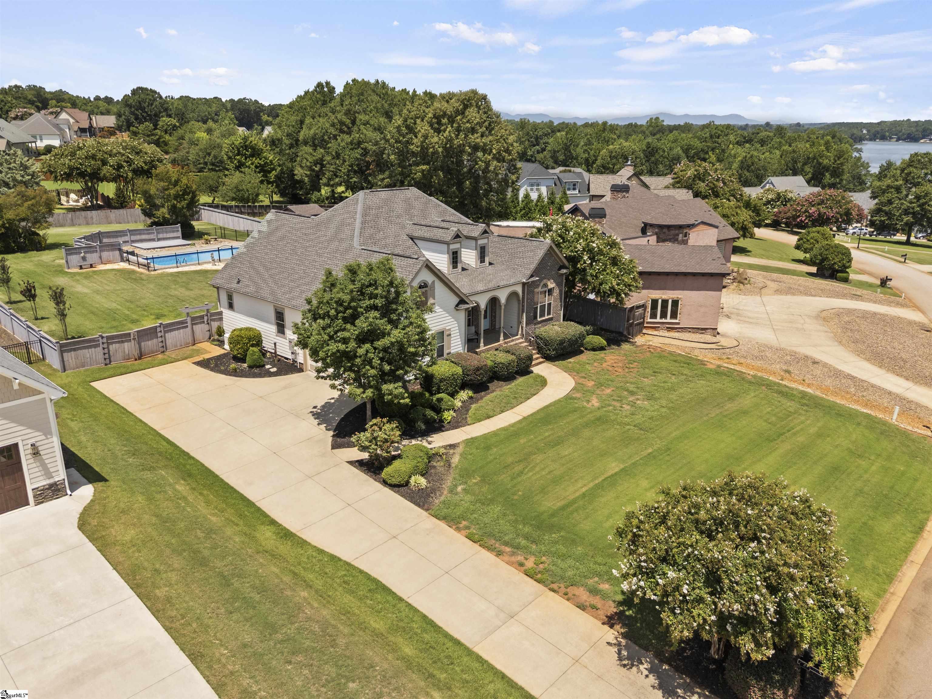 Aerial view of a light-sided home with a fenced backyard pool, landscaped lawn, and broad driveway.