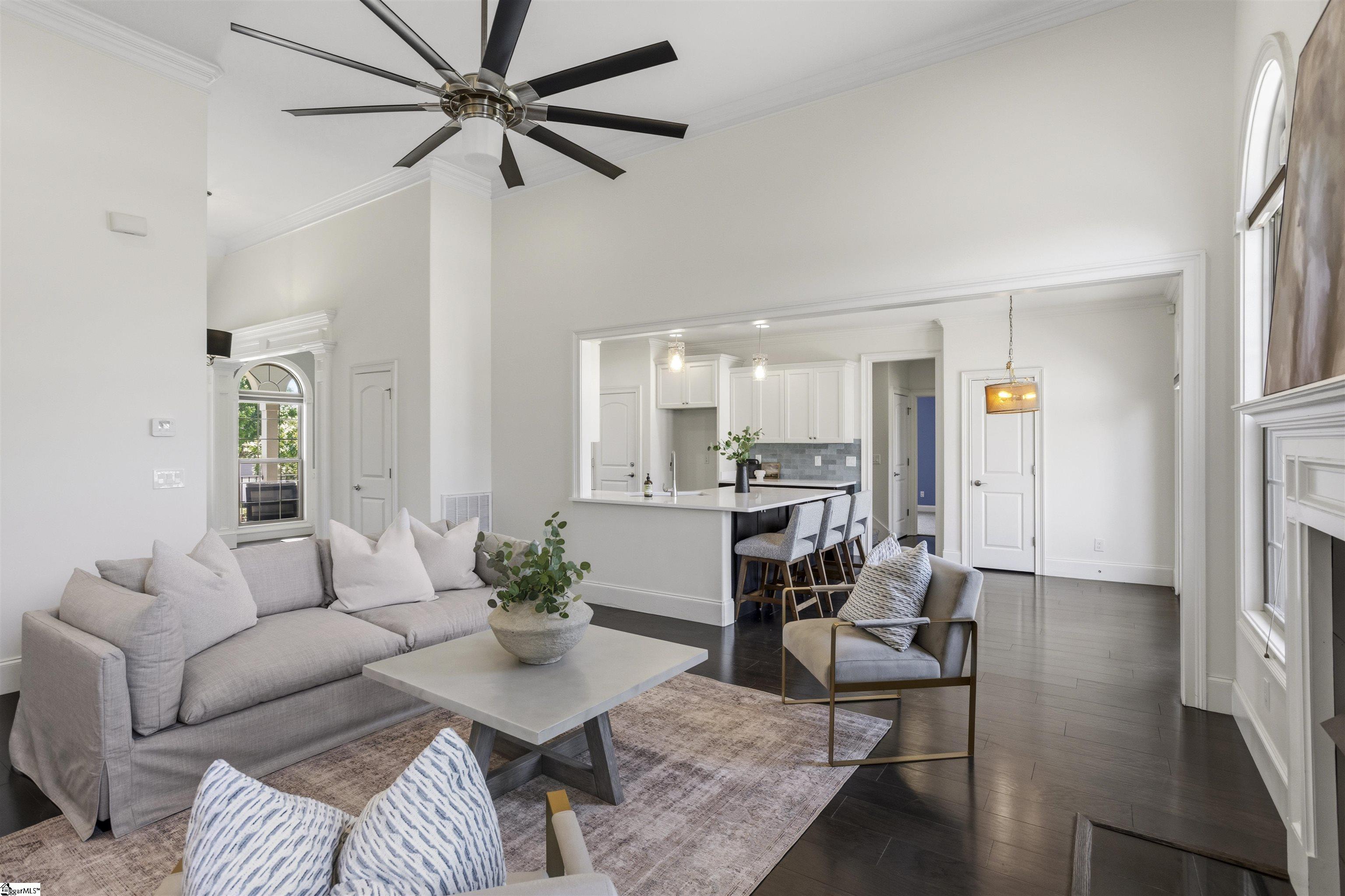 Staged living room with gray seating, dark hardwood floors, and an open kitchen with island.