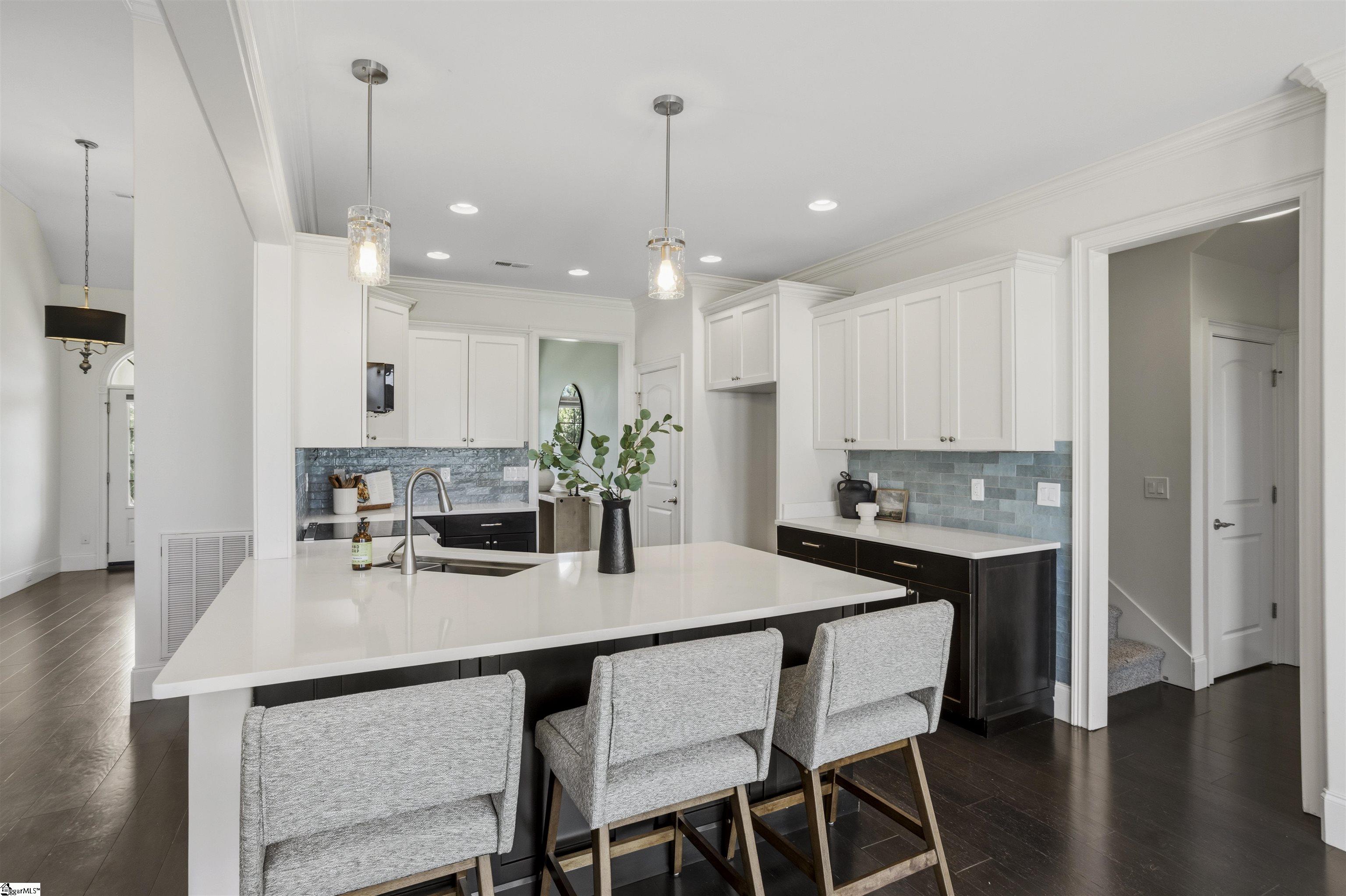 Kitchen with a large white island, blue tile backsplash, and three gray bar stools.