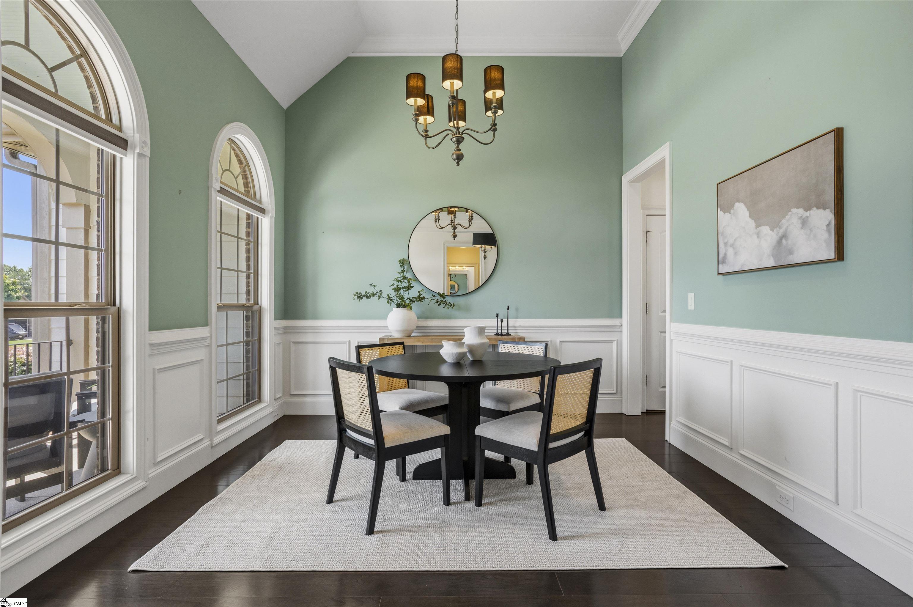 Dining room with a round black table, arched windows, mint-green walls, and white wainscoting.