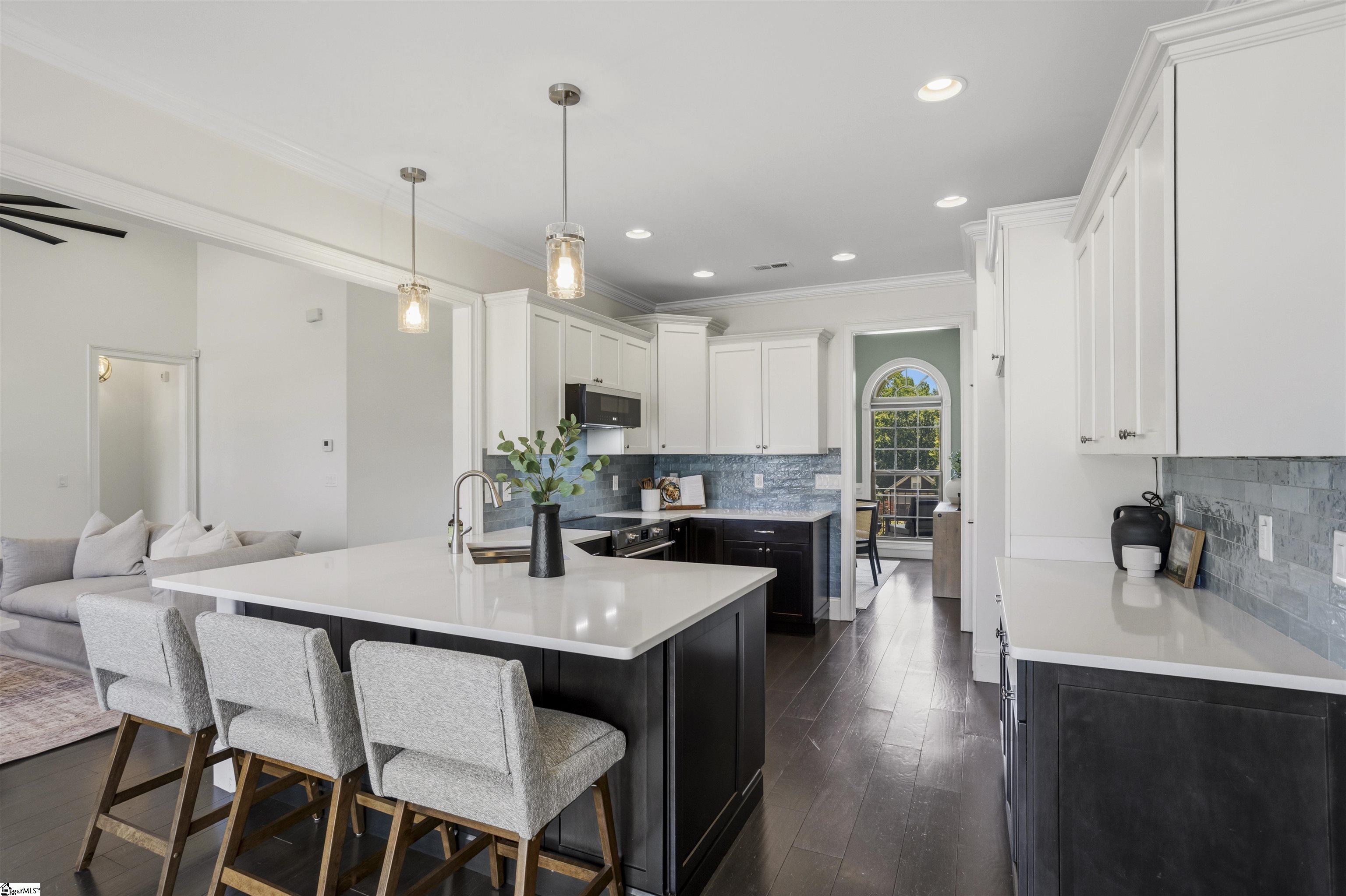 Kitchen with a large white island, dark cabinetry, blue-gray backsplash, and upholstered breakfast bar stools.