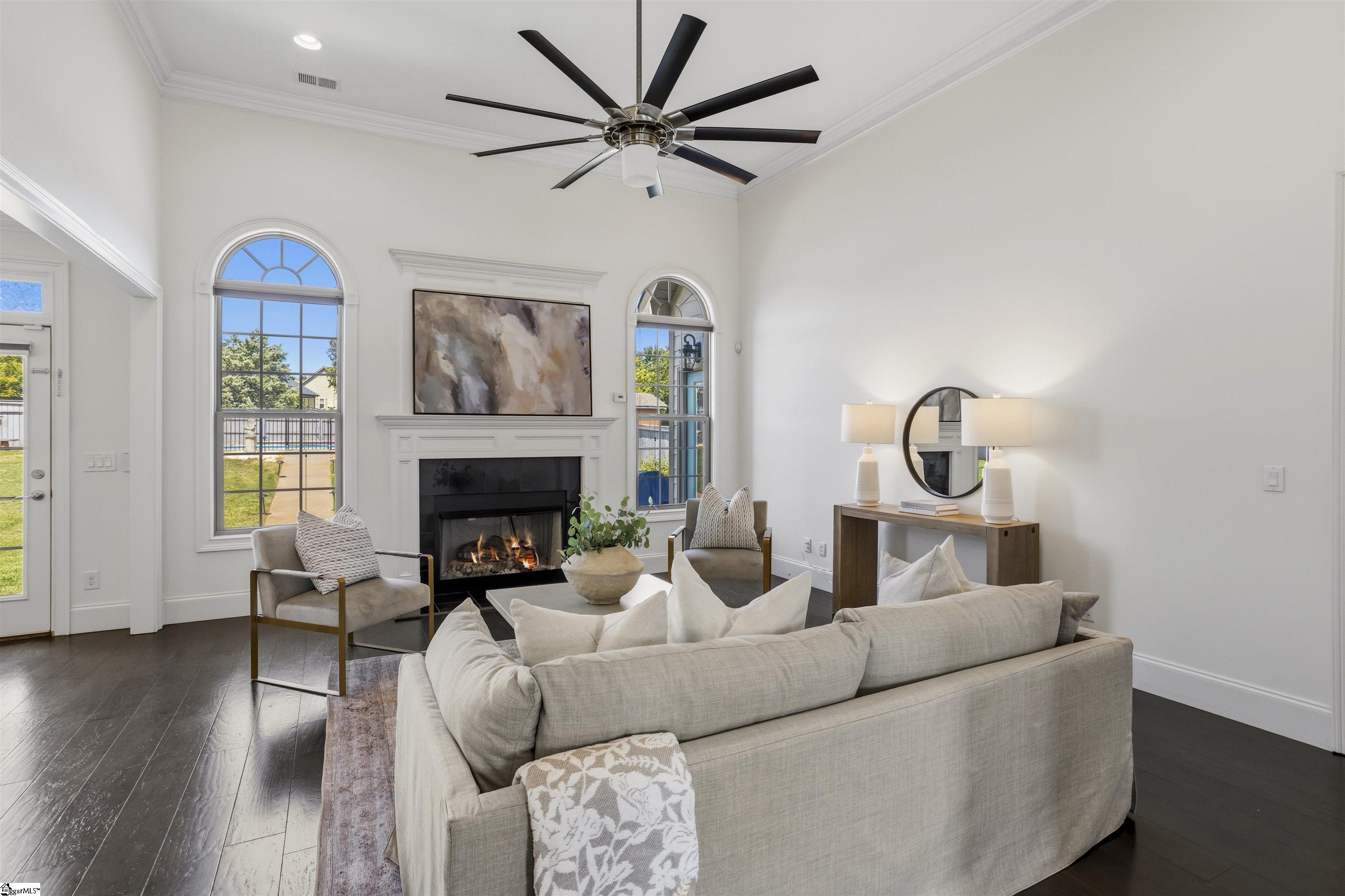 Living room with a white fireplace, arched windows, neutral furnishings, and dark hardwood floors.