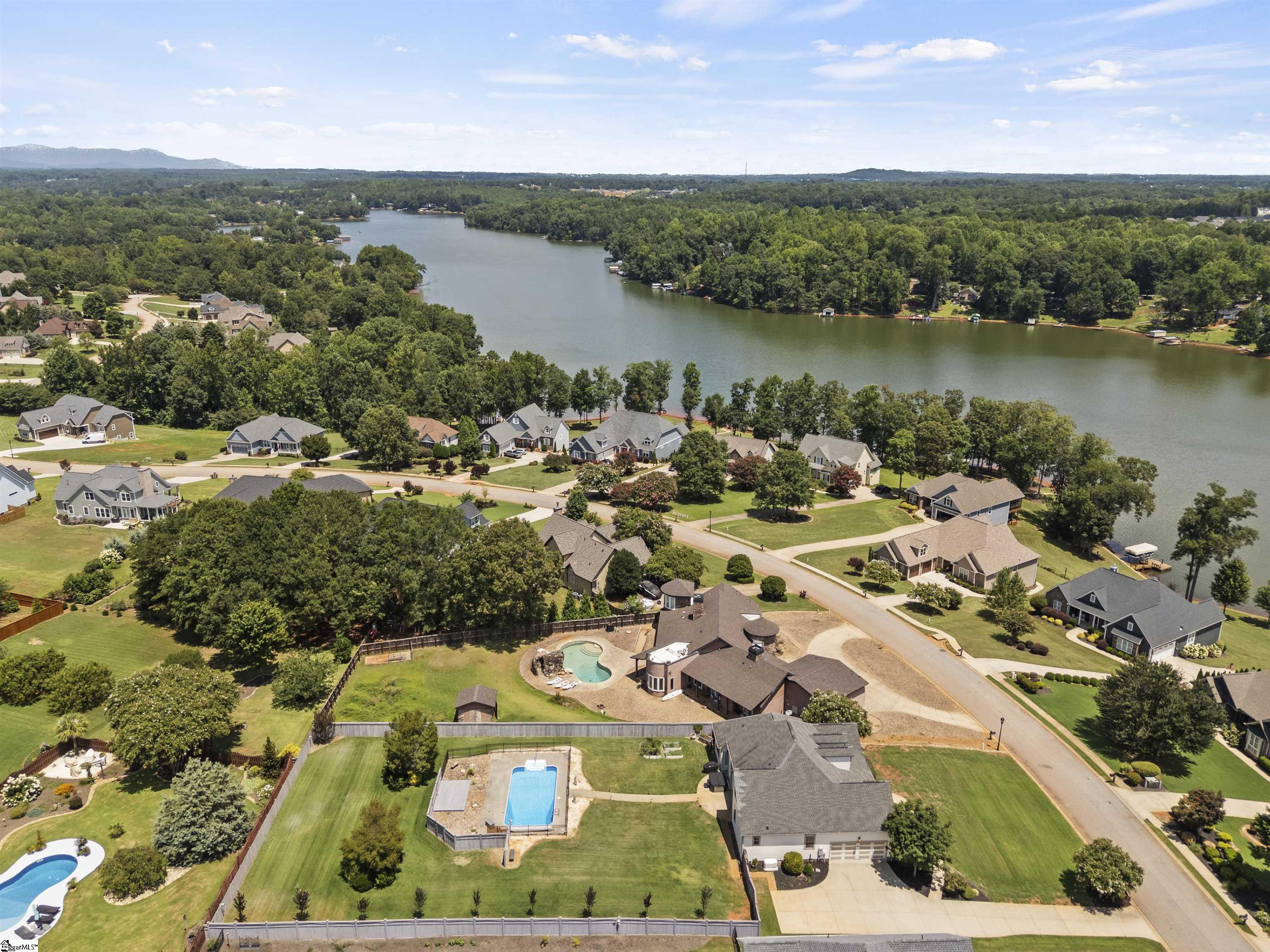 Aerial view of homes and swimming pools beside a broad, tree-lined lake.