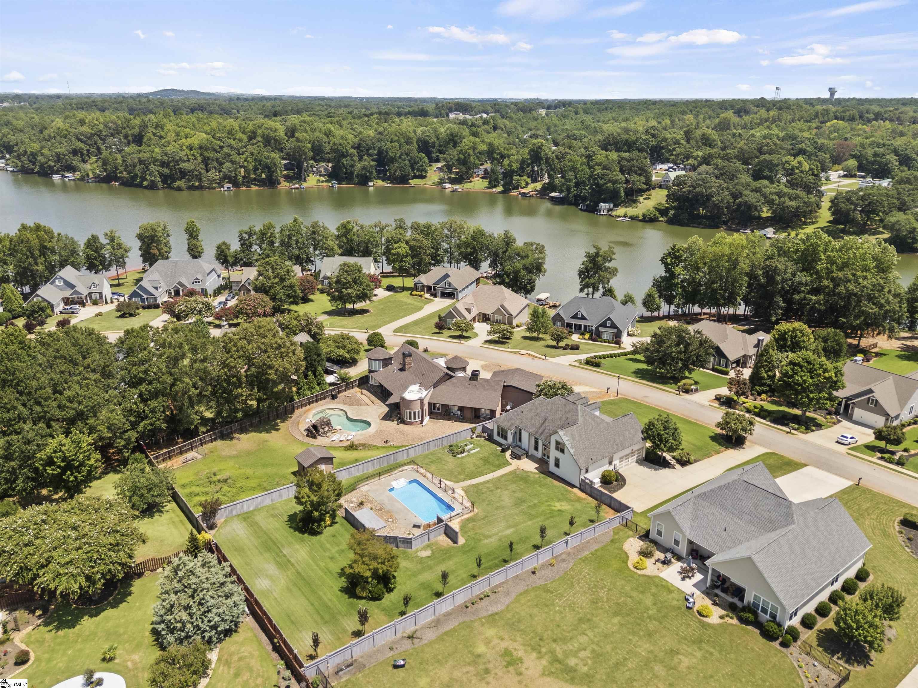 Aerial view of lakefront homes, wooded shoreline, and fenced yards with swimming pools.