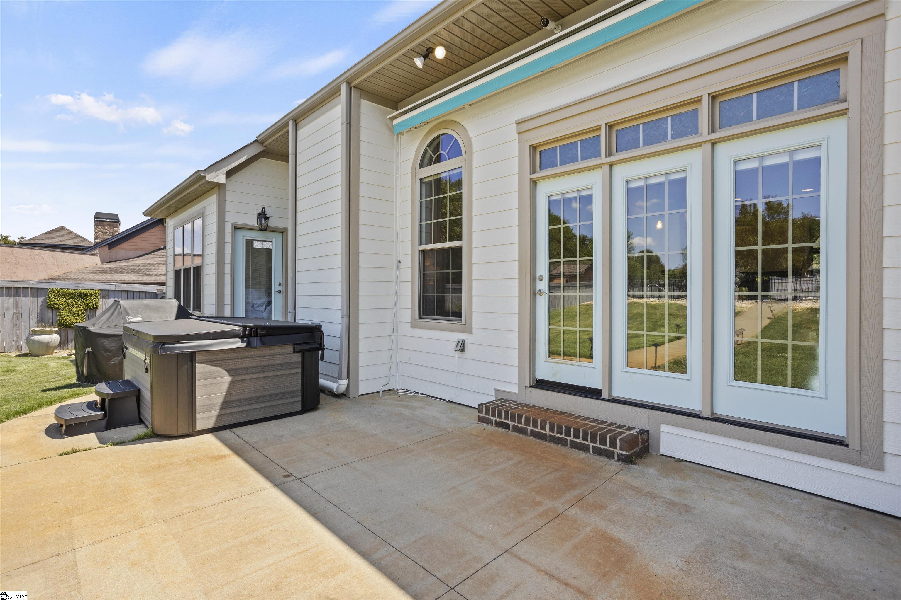 Covered patio with a hot tub beside pale blue French doors and an arched window.