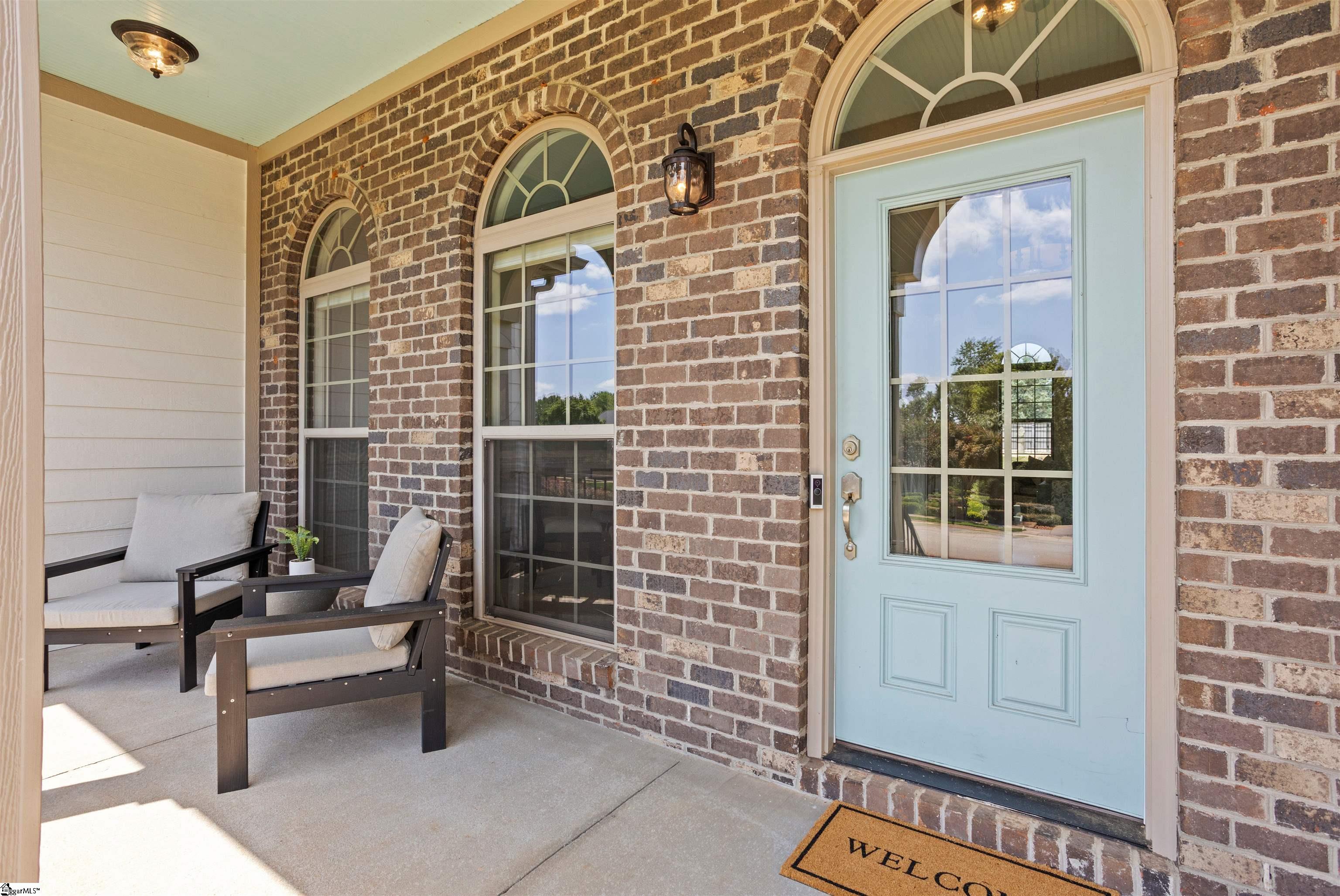 Brick front porch with a pale blue entry door, arched windows, and two cushioned chairs.