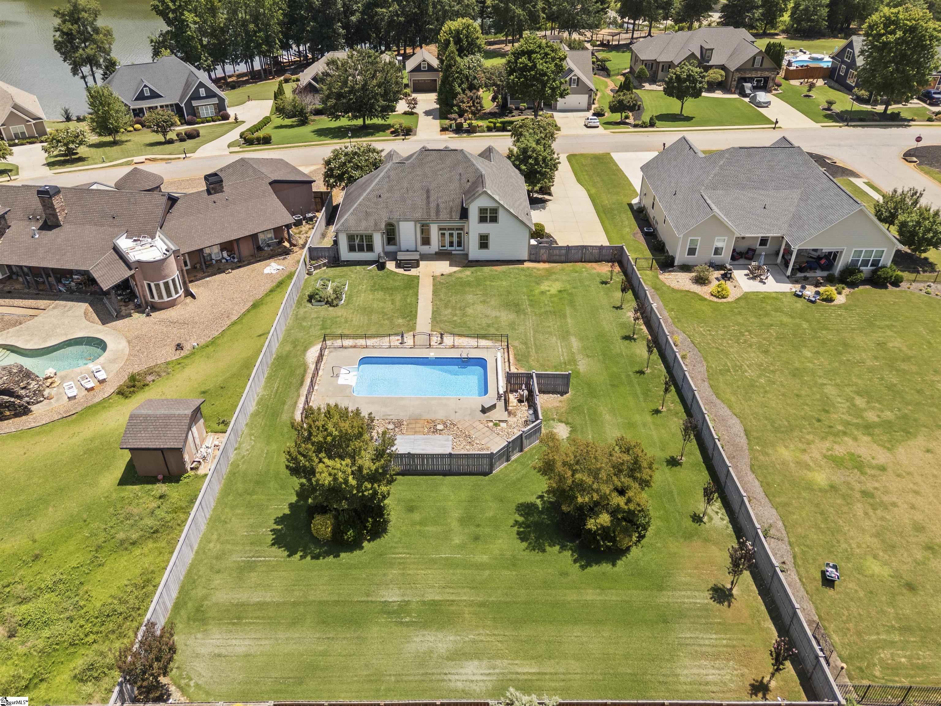 Aerial view of a home with a fenced lawn and swimming pool beside a lake.