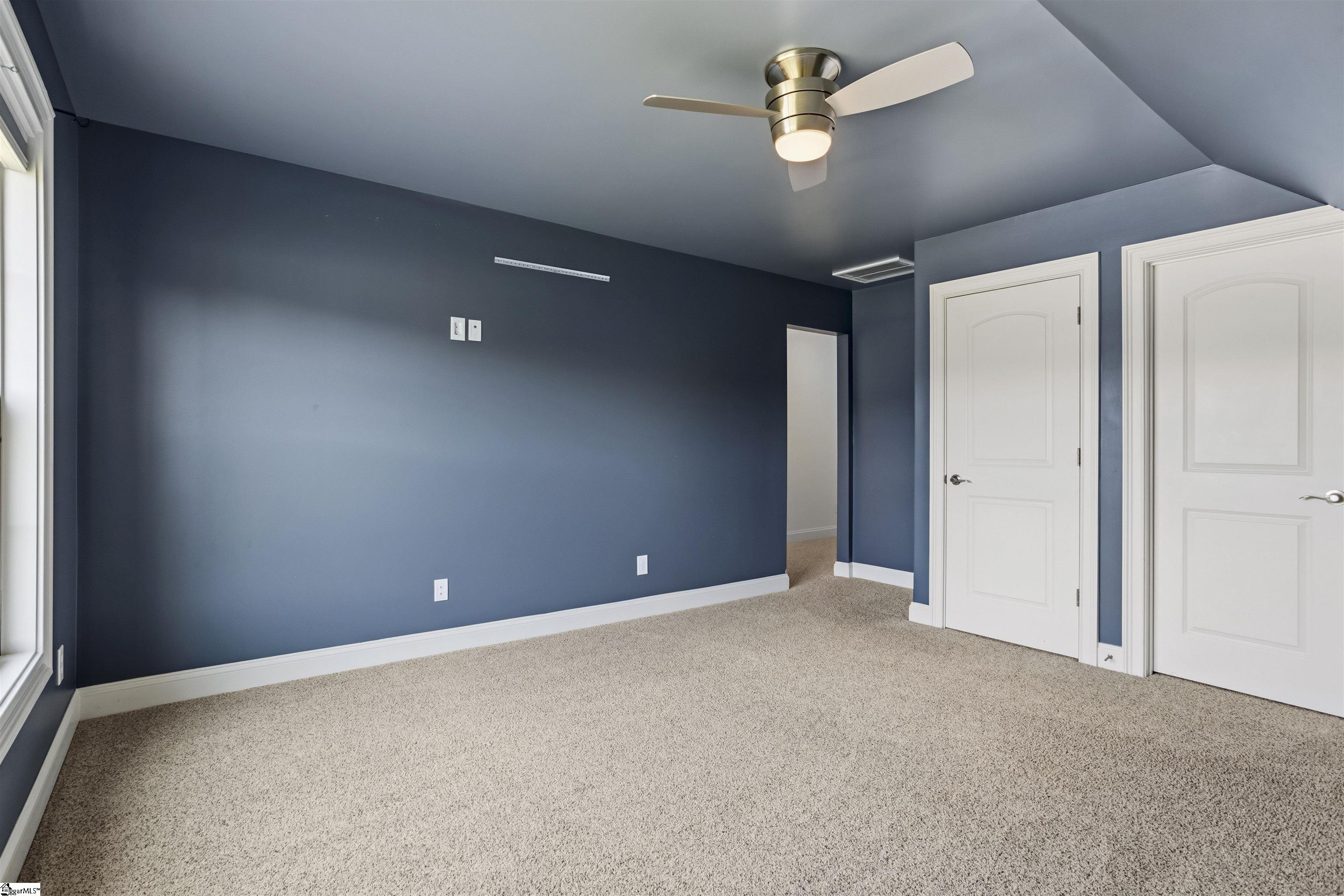 Unfurnished bedroom with dark blue walls, beige carpet, a ceiling fan, and two white doors.