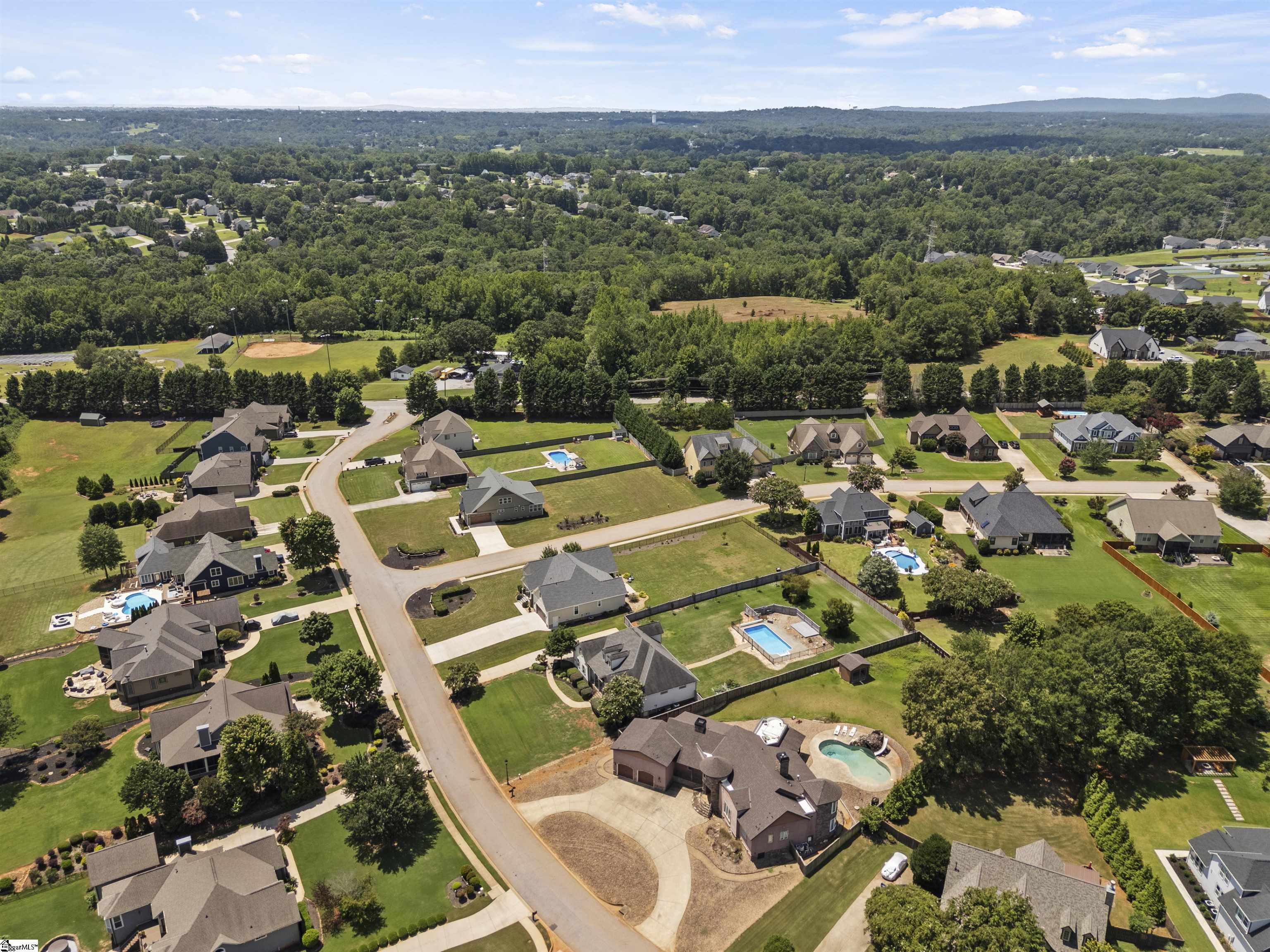 Aerial view of a wooded neighborhood with detached homes, spacious yards, and several swimming pools.