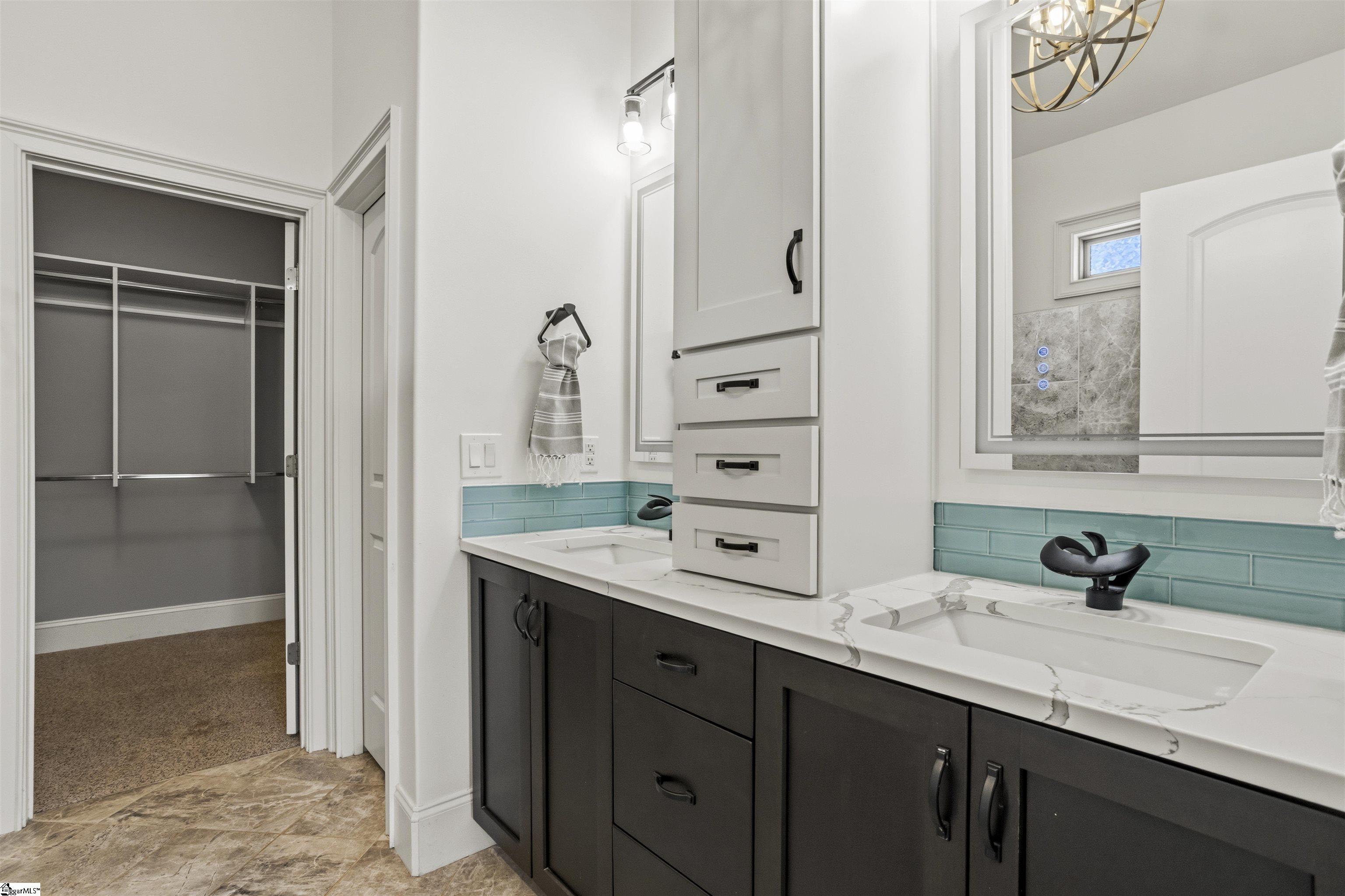 Bathroom with a double vanity, turquoise tile backsplash, and an open doorway to a walk-in closet.