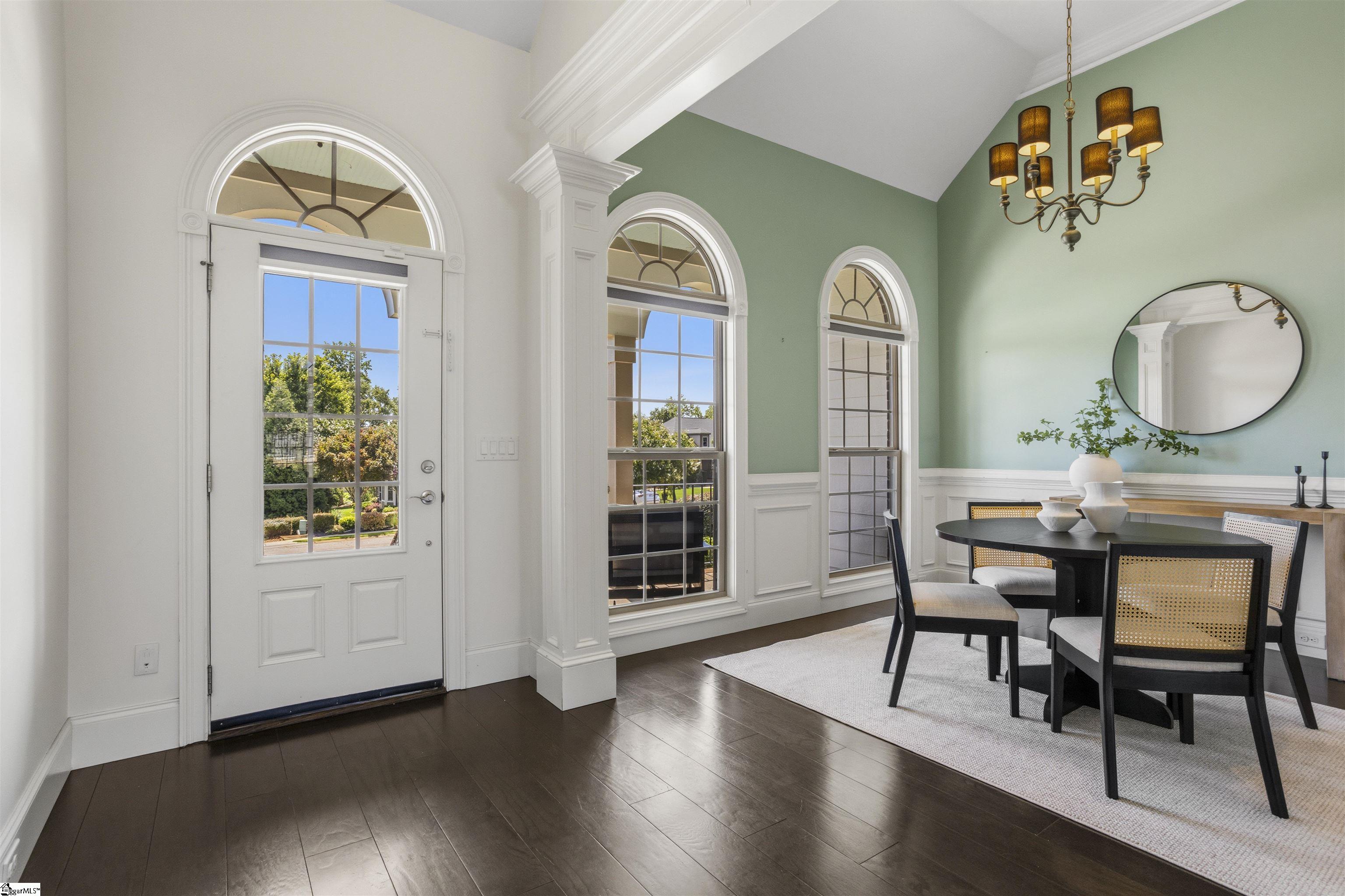 Dining area with a black table, pale green wall, and tall arched windows beside the front door.