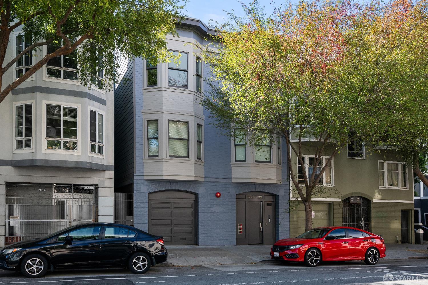Blue-gray San Francisco building with bay windows and garage, framed by leafy street trees.