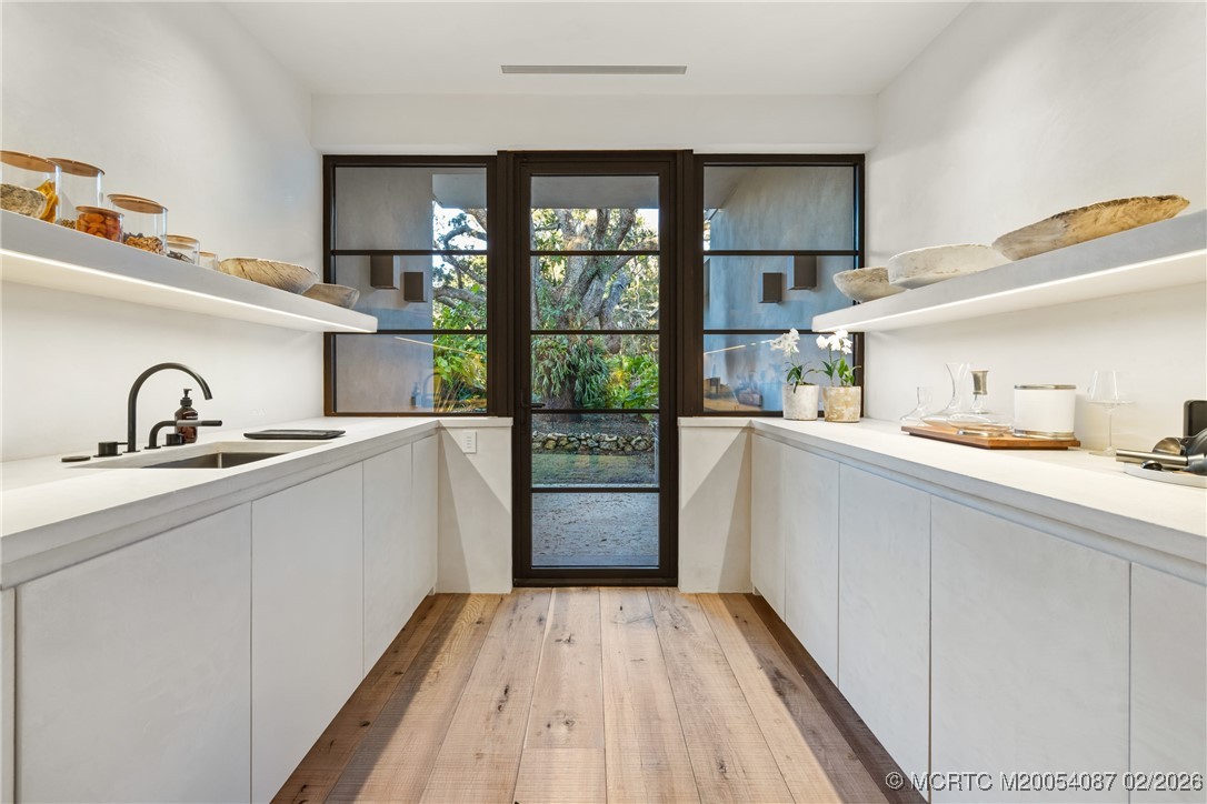 White butler’s pantry with a black faucet, open shelves, and a glass door facing greenery.