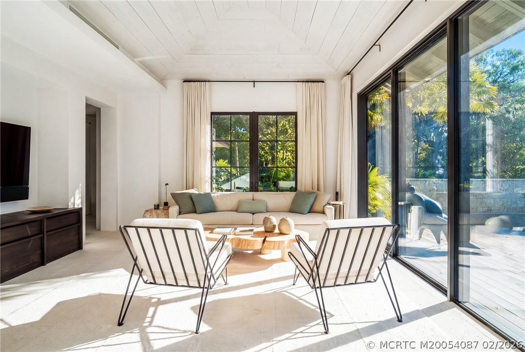 Bright living room with cream seating and large glass doors opening onto a tropical patio.