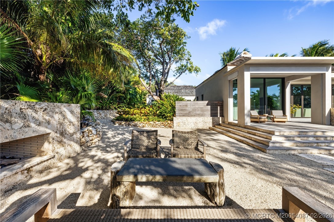 Modern home patio with lounge seating, stone steps, and lush tropical landscaping.