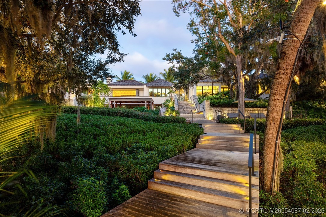 Modern home reached by illuminated steps through lush tropical landscaping.