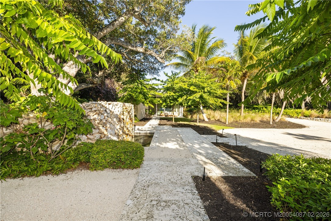 Stone walkway leading to the home, framed by a low stone wall and tropical palms.