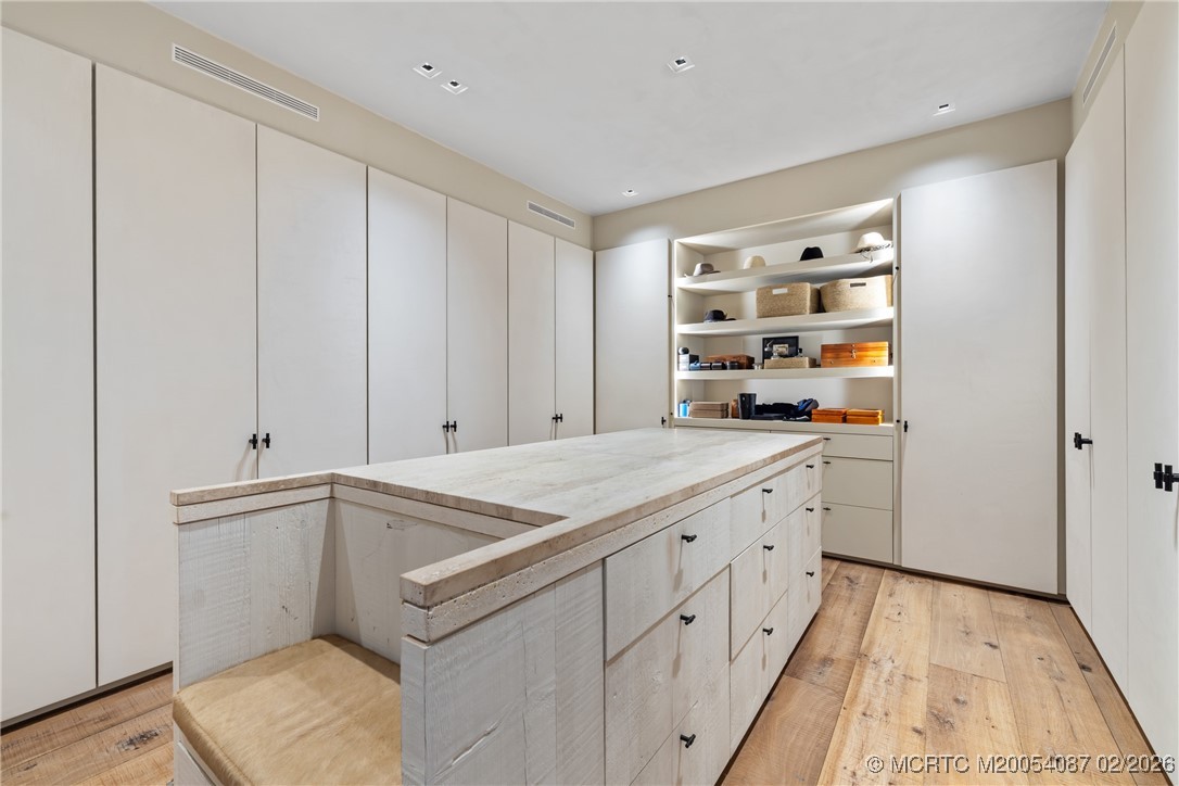 Walk-in closet with a large central island, white cabinetry, and open display shelves.