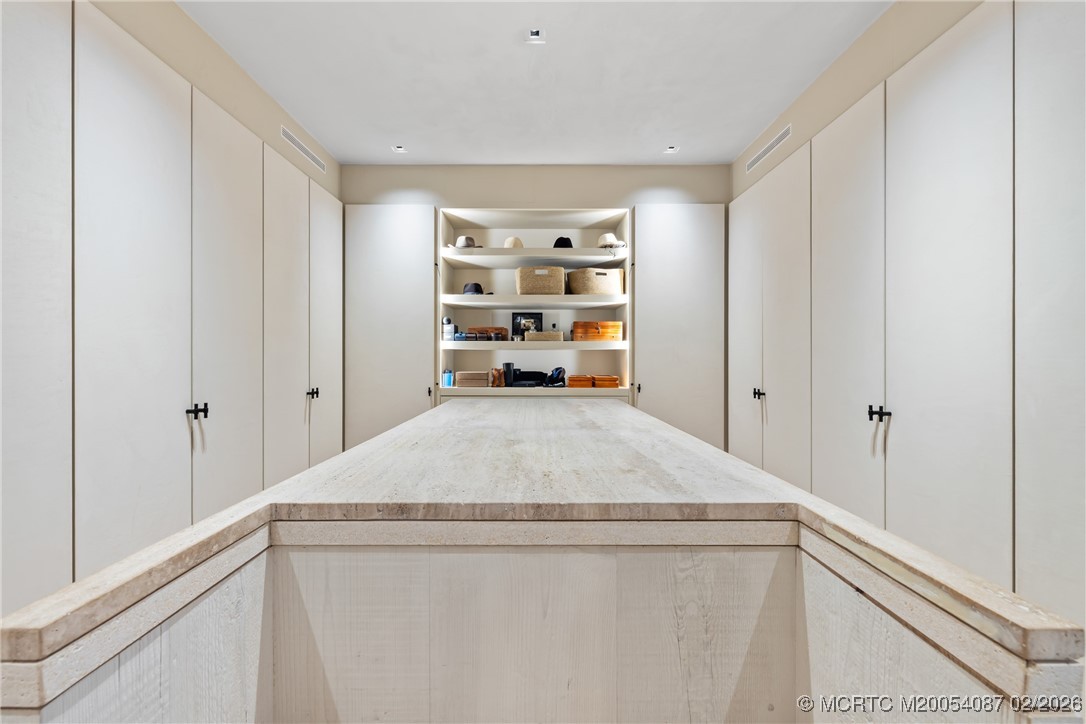 Walk-in dressing room with a stone-topped island and white built-in cabinets.