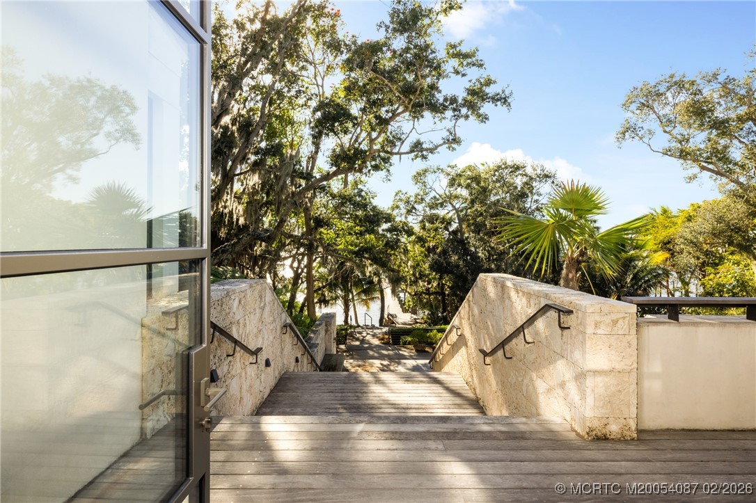 Wooden steps descend between stone walls and mature trees toward the water.
