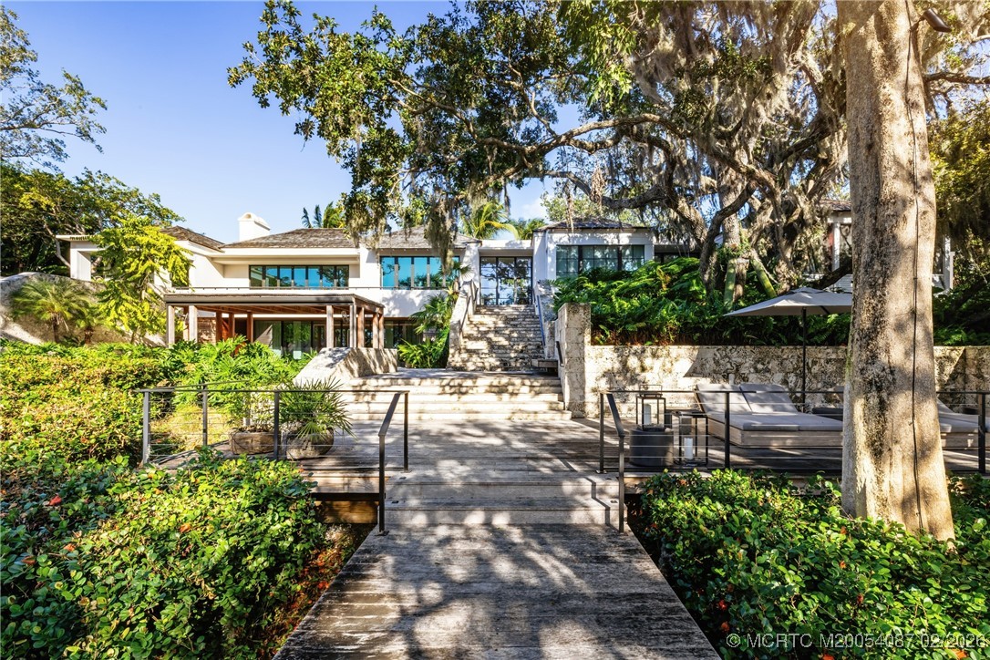 Modern white home with tiered stone stairs, a broad walkway, and mature trees.