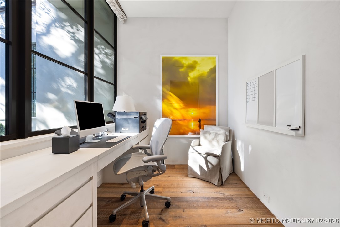 Bright home office with a long desk, tall black-framed windows, and a sunset artwork.