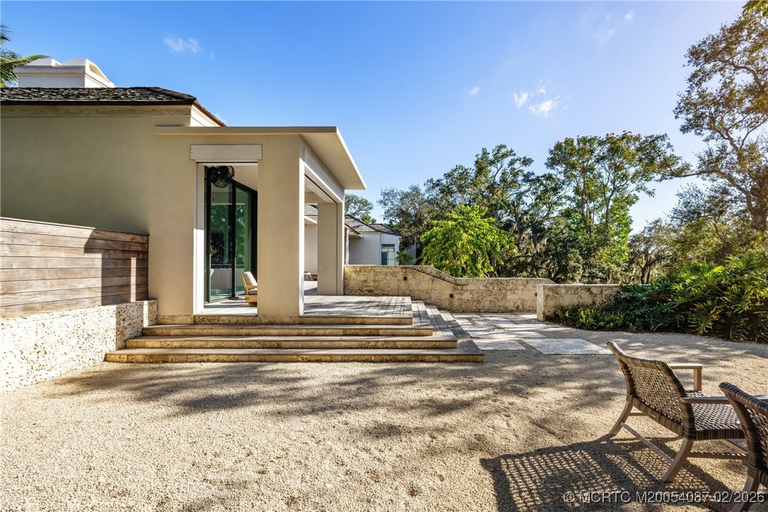 Modern home exterior with a broad stone patio, shallow steps, and wicker chairs.