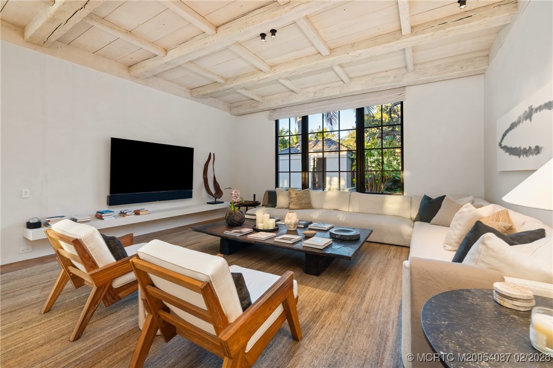 Living room with a white sectional, wood lounge chairs, and a white beamed ceiling.