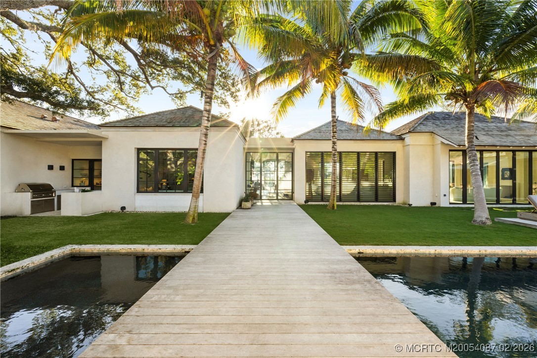 Modern white home with a broad dock across the water, palm trees, and manicured lawn.