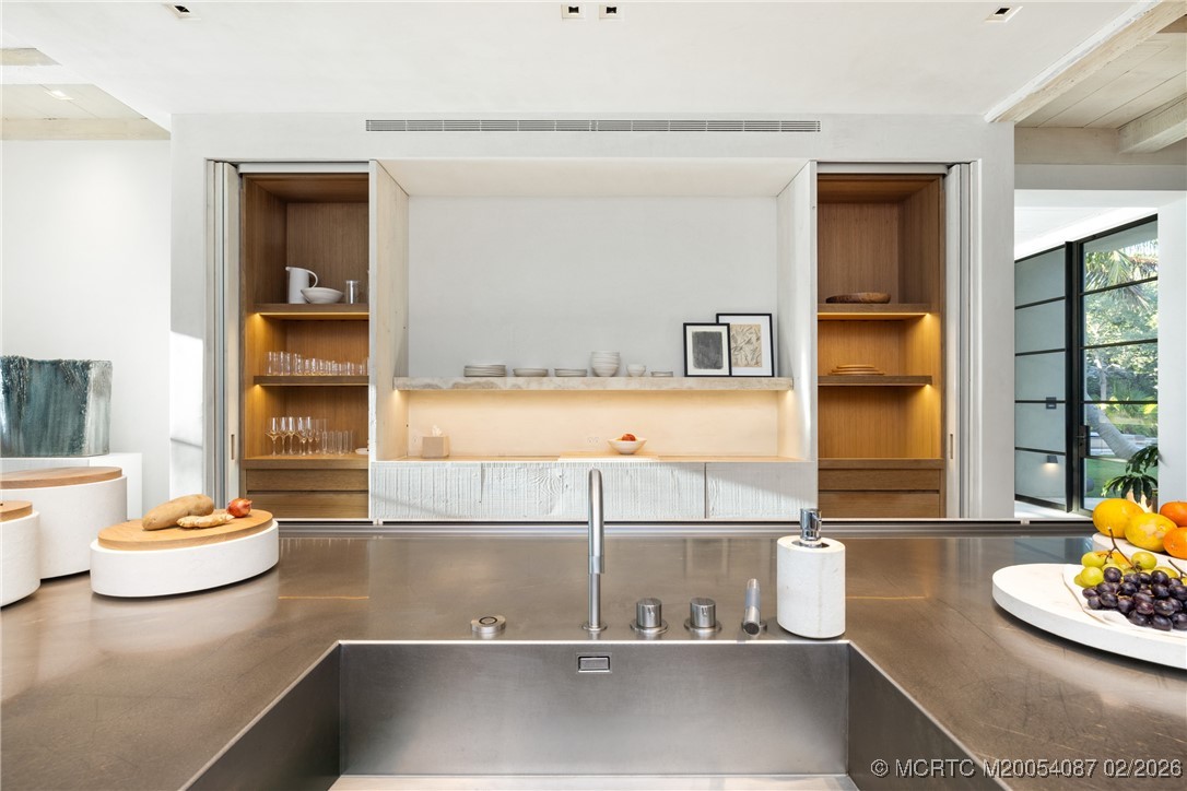 Modern kitchen with a stainless-steel island, integrated sink, and illuminated wood display shelves.