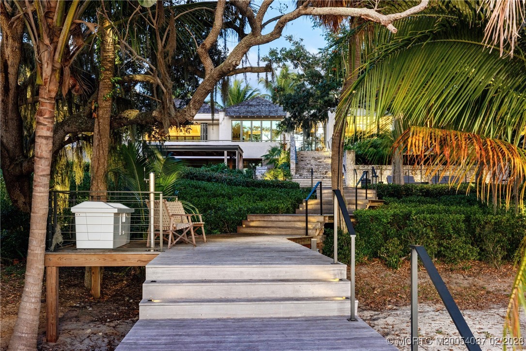 Modern white house beyond a wooden walkway and steps framed by tropical palms.