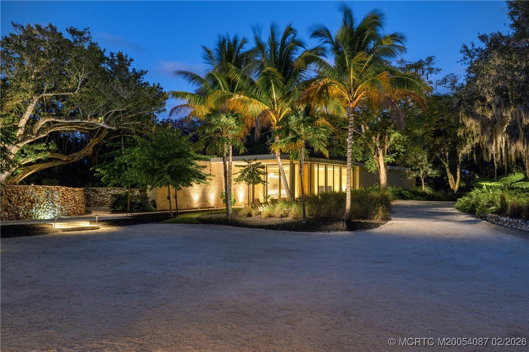 Modern home entrance illuminated at dusk, framed by palms and tropical landscaping.