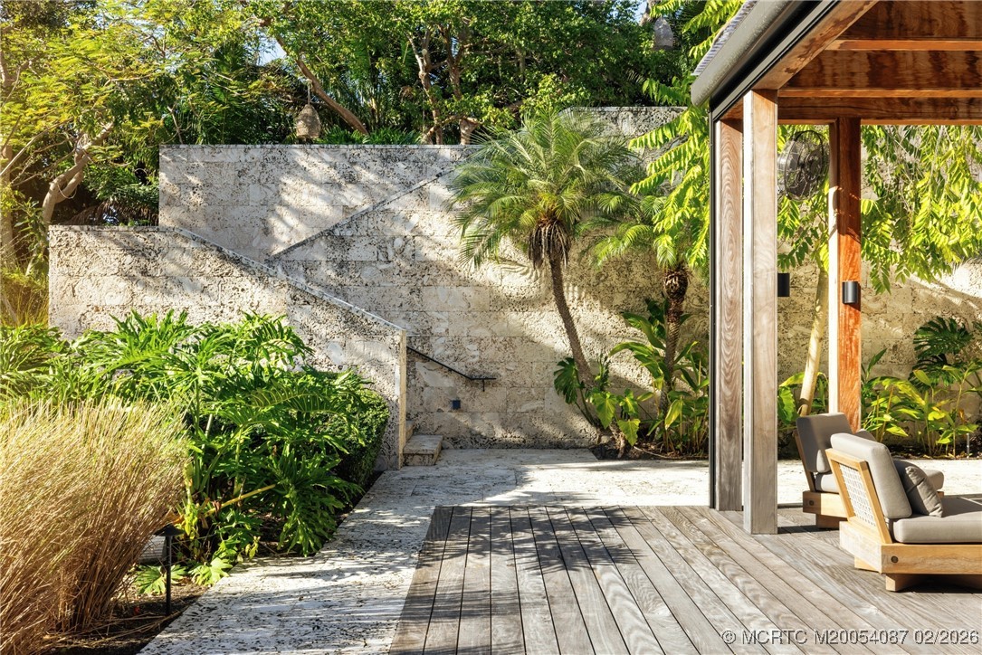 Outdoor patio with a timber pergola, wood deck, stone steps, and lush tropical landscaping.