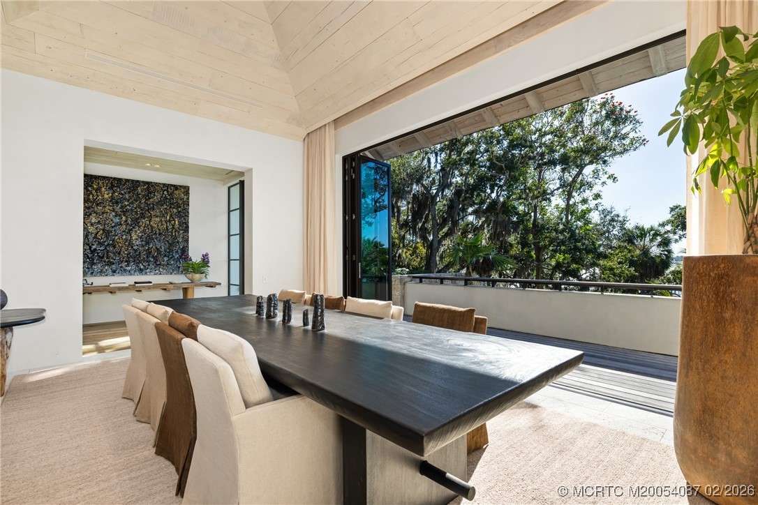 Dining room with a long dark table opening onto a covered deck beneath the trees.