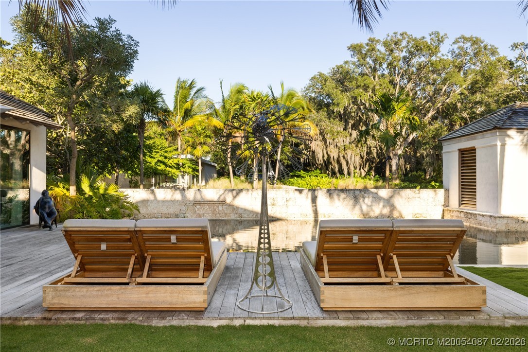 Outdoor pool patio with paired wooden loungers, a metal sculpture, and tropical landscaping.