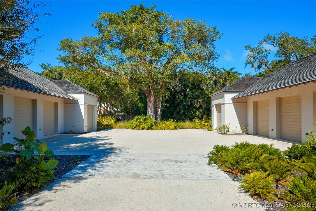 Paved courtyard between white garage wings, framed by tropical landscaping and a large shade tree.