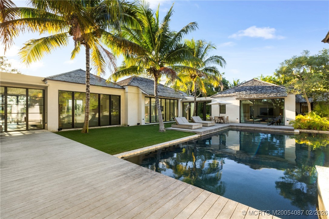 Modern home surrounding a swimming pool, with a broad wood deck, palm trees, and poolside loungers.