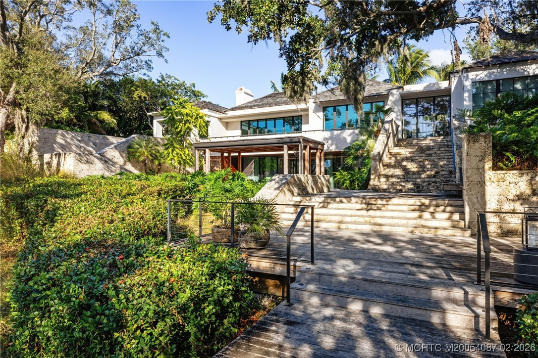 Modern white home with broad stone stairs, a wooden deck, and tropical landscaping.