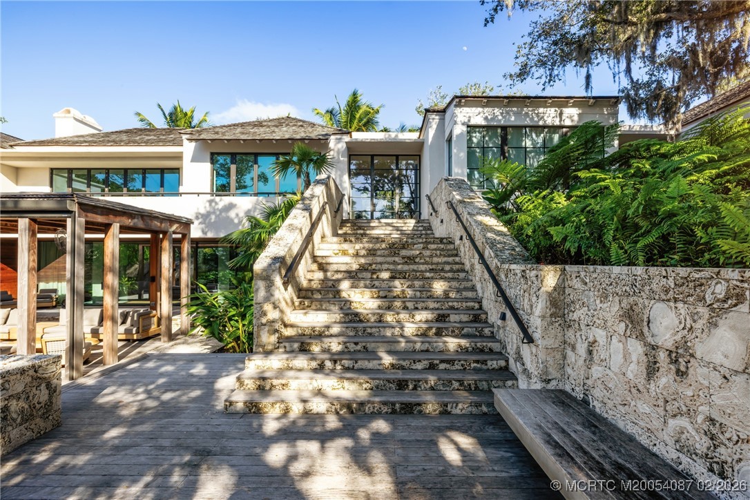 Modern home entrance with broad stone stairs, tropical landscaping, and a covered patio.