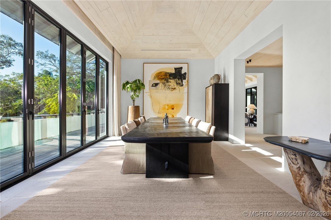 Dining room with a long dark table, abstract artwork, and glass doors overlooking trees.