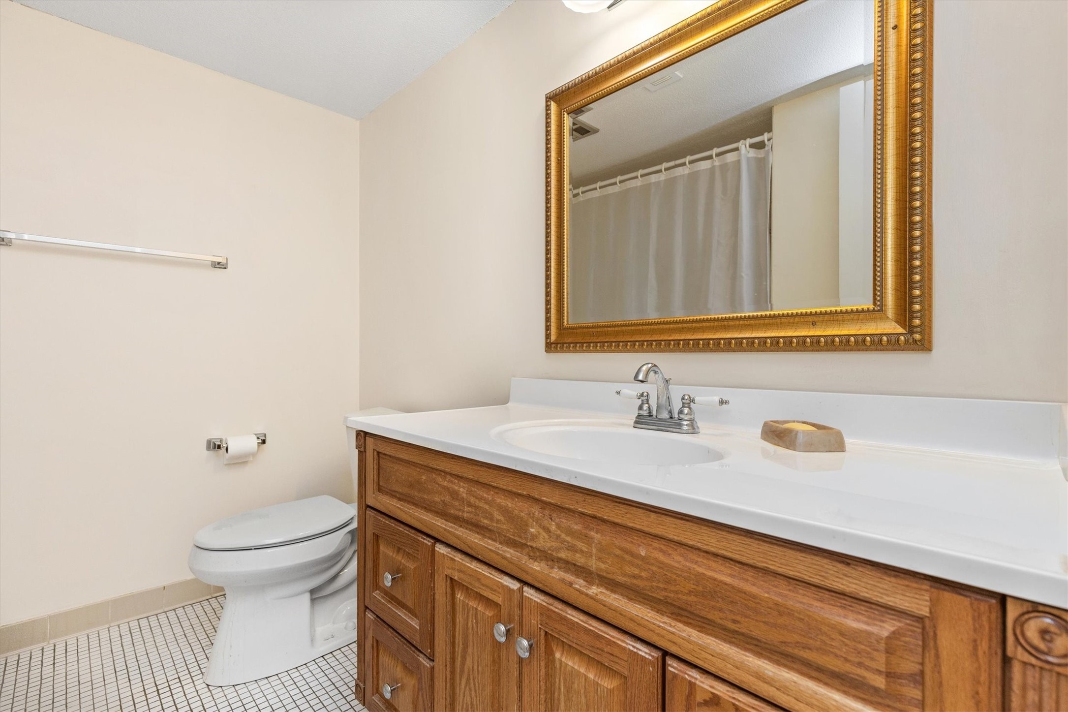 Bathroom with a wood vanity, white sink, ornate gold-framed mirror, and tiled floor.