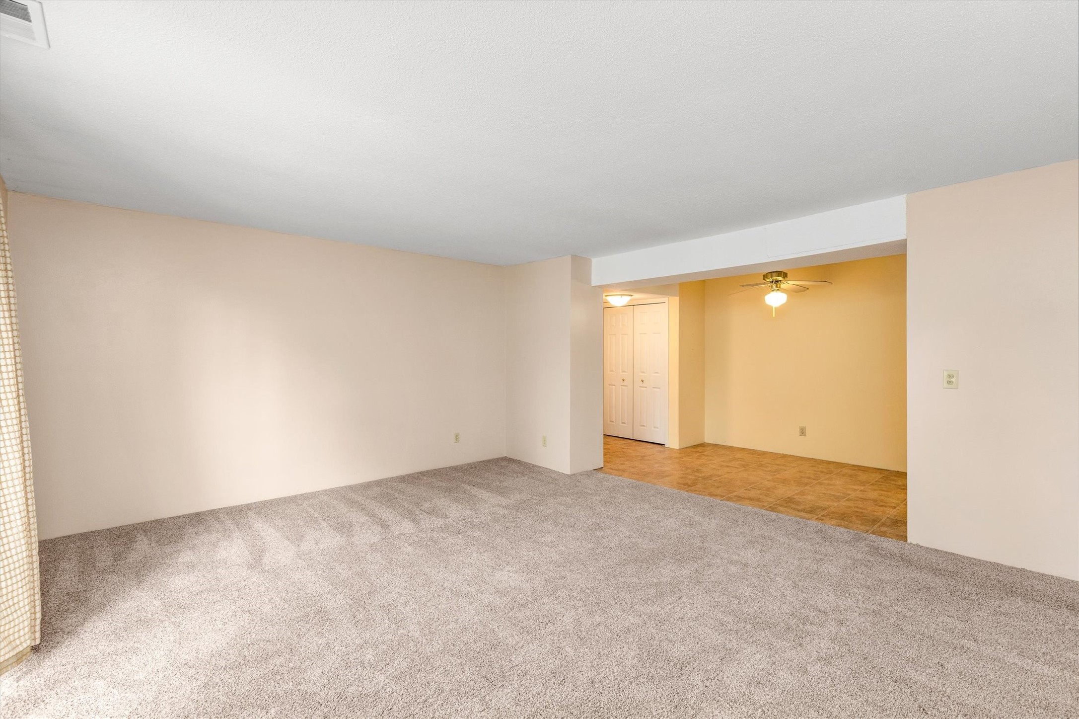 Empty living room with gray carpet opening onto a tiled area and double closet doors.