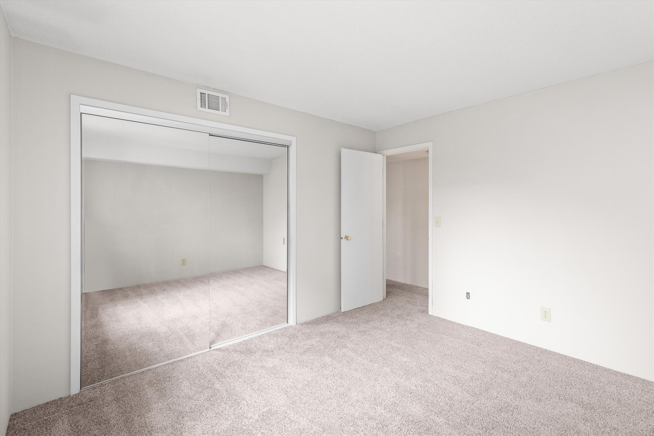 Empty carpeted bedroom with a large mirrored sliding-door closet.
