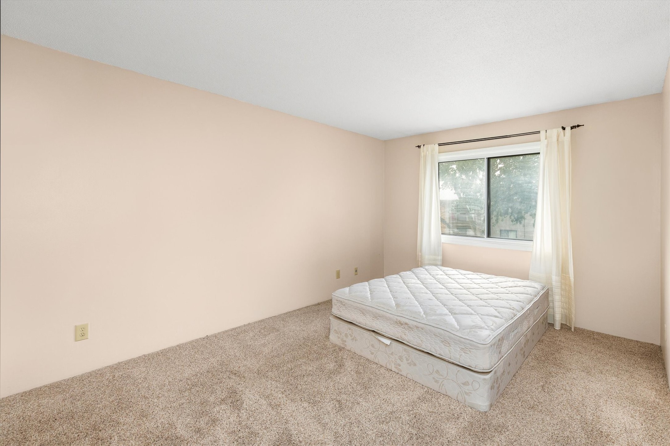 Bedroom with a mattress on the carpet beneath a curtained window.